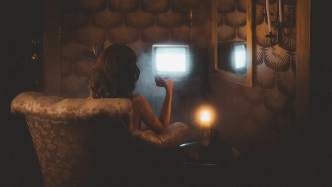 A woman in an armchair watches a small glowing TV by candlelight, the kind of evening viewing an IPTV app like IPTV Smarters Pro is for