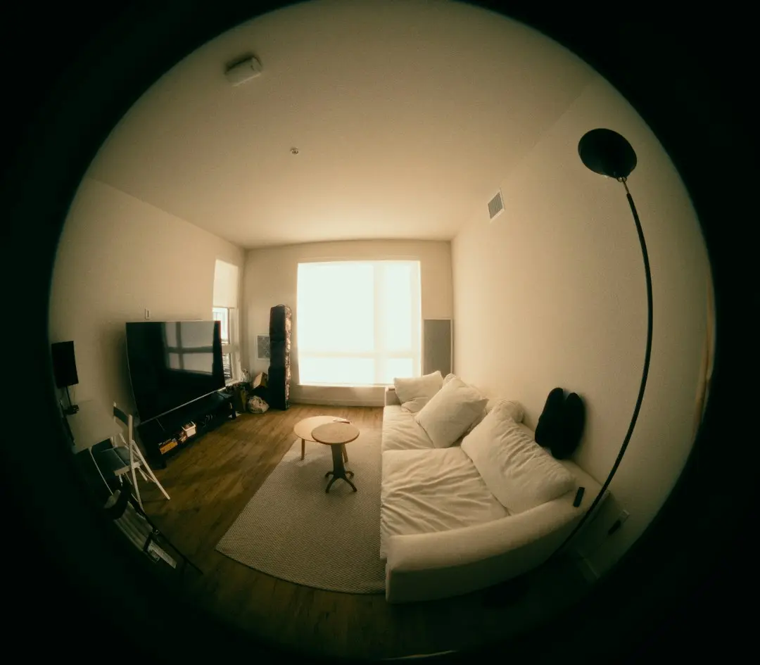 A fisheye view of a bright living room with a large TV, a white sofa and a floor lamp, the kind of room IPTV Free Trial streams to